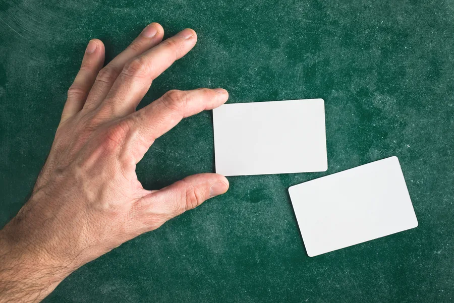 Mano que sostiene una tarjeta PVC blanca con esquinas redondeadas junto a otra tarjeta sobre un fondo verde
